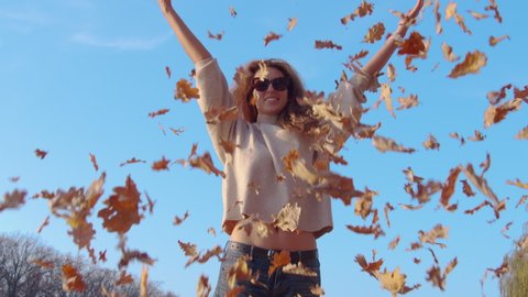 Girl tossing colorful autumn foliage up in air in park.