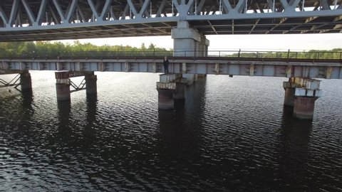 A businesswoman in a suit is standing on the edge of a bridge ready to jump down.  A lonely girl stands on the edge before a cliff in the water and looks into the distance. Aerial, Drone 4K. 