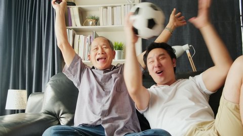 Two generation, father and son watching football, soccer on television together. Grandfather, man holding football sitting on sofa feeling excite and happy when team they cheer goal and score success.