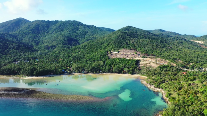 Beautiful shoreline of tropical island with coral barriers, turquoise shallow lagoon and rocks under green sharp slopes of hills in koh phangan, Thailand