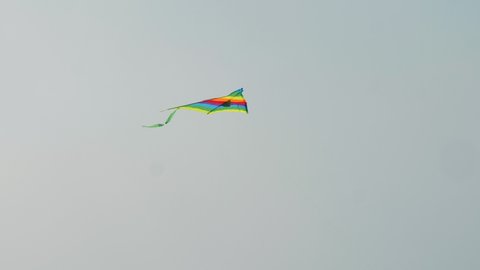 colorful red green and yellow kite with wide stripes and tail flies in clear blue sky on hot summer sunny day. Concept beach leisure