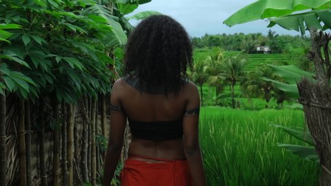 Video of a beautiful young brunette Africa girl with makeup and painted etрnic lines on the body walking in a tropical garden