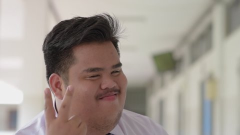 A fat Asian man wearing an office suit and wearing a necktie and a white shirt, making a cheeky, funny, good-humorous gesture.