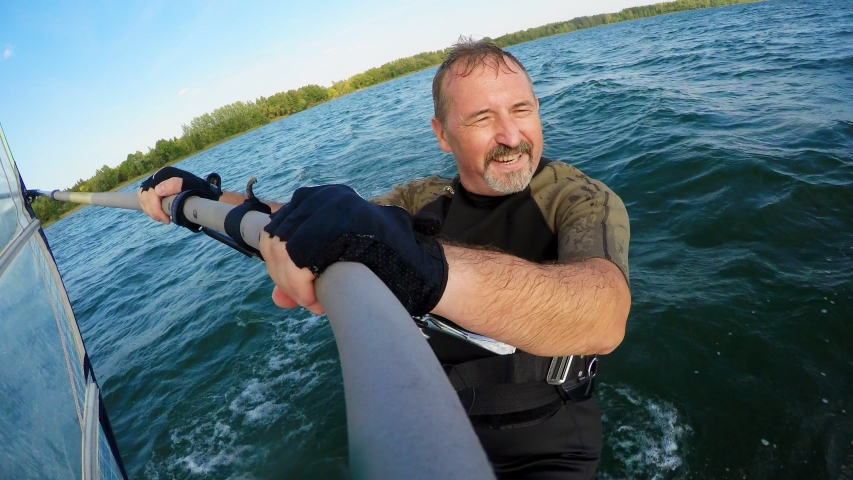 Bearded man does sailing on a windsurfing board on a beautiful lake