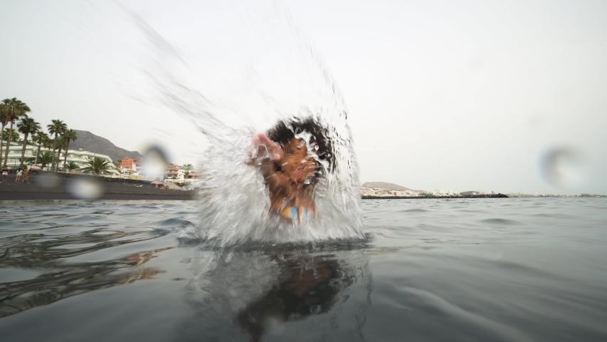 Afro kid splashing water on camera while swimming inside the ocean during summer vacation - African child having fun playing on the beach - Youth, lifestyle and happy people concept