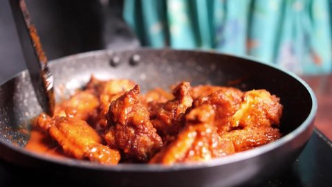 Closeup of hot and spicy buffalo chicken wings being stirred in a non-stick pan