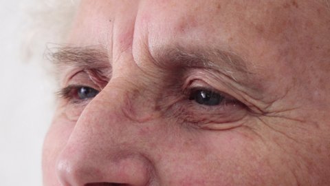 Eyes blinking and wrinkles on face of elderly sad thoughtful woman, closeup