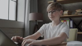 teenager with glasses waves his hand at a laptop, talking via video calling