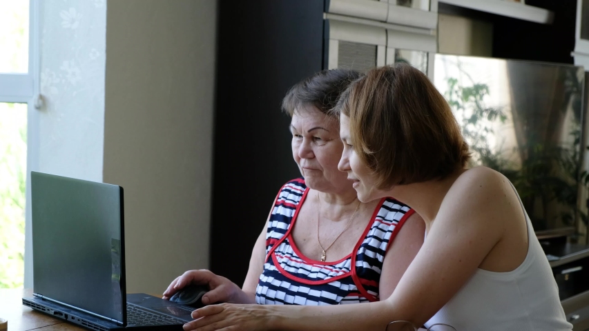 Adult daughter helping senior woman, her mother, with a computer laptop