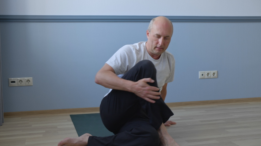 Man practicing yoga and sitting in twist pose at home. Athletic focused middle aged man in sportswear sitting on mat and practicing yoga during indoor training