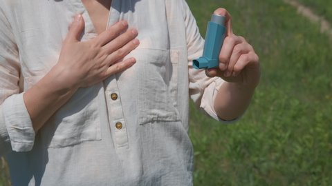 Asthma attack. A woman with hard breathing use inhaler in the park. A concept of asthma attack in nature.