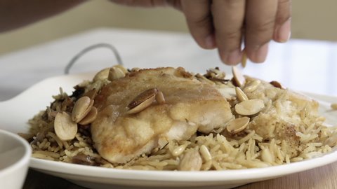 Sprinkling almond nuts on a plate of roasted fillet fish with spiced rice, middle eastern cuisine