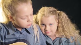Two young beautiful sisters with wavy hair learn to play the guitar.