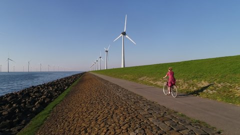 WS AERIAL POV TS SLO MO Girl cycling on road along wind farm / Urk, Flevoland, Netherlands