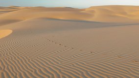 Abstract rippling texture on the desert surface. 4K drone view over the scenic massive golden dunes and blue sky above. Beautiful aerial video of wild nature landscape at sunrise, California, USA
