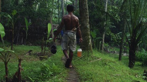 Farmer takes coconut nectar to grass hut in jungle permaculture farm in Bali