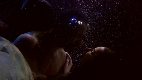 man and woman are having sex underwater, floating in dark water in deepness