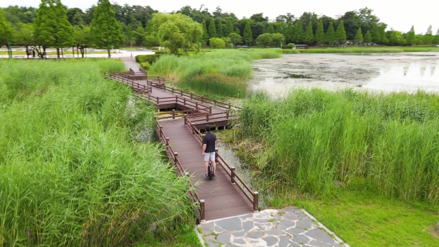 A man in sneakers rides an electric unicycle on wooden bridge on background of green grass