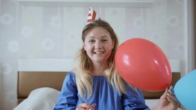 15 virtual parties, cheerful girl with balloons and hat wishes her friend happy birthday online on webcam on laptop with self-isolation on carnitine sitting at home on bed, social distance