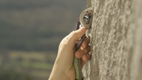 SLOW MOTION, CLOSE UP, DOF: Rock climber clips a carabiner into a bolt screwed into the cliff. Lead climber quickdraws a carabiner into a bolt. Unrecognizable fit woman clips carabiner into a bolt.