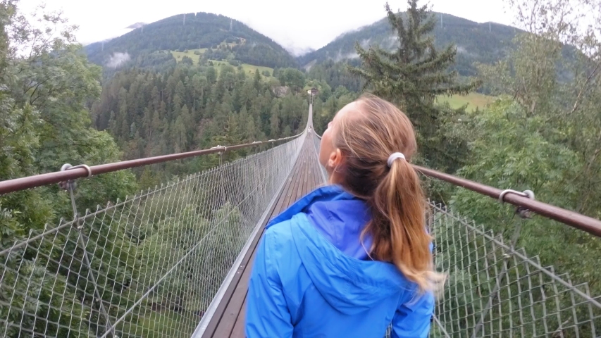Woman walking on suspension bridge over pine tree valley in Switzerland