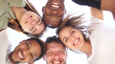 Close portrait of five young students, tolerance and no racism concept. Interracial group of students leaned over the camera against the sky