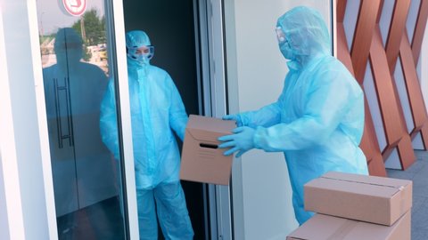 Delivery of parcels with medical equipment or drugs to hospital during coronavirus outbreak. Courier, in protective suit, is handing cardboard boxes to nurse. Cargo delivery service during quarantine.