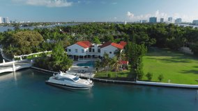 Expensive home with yacht at the private pier, USA. 4K aerial close view on Star Island with Miami downtown on a background. Lavish nature of a green tropical island. Stock video for travel business.