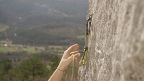 SLOW MOTION, CLOSE UP, DOF: Unrecognizable female climber hooks a carabiner into metal bolt and attaches her belay rope. Woman lead climbing attaches a carabiner and belay rope while climbing up cliff