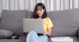 Young asian woman wearing headphones having video chat with friends using laptop camera while siting on couch at the living room, Online meeting in video call for social distancing.