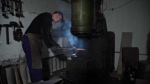 Blacksmith Shaping Piece of Hot Metal Using Forging Press at Workshop of Forge Factory. The Process of Making Blades for Knifes and Steel Arms