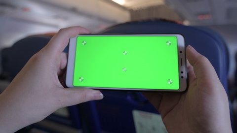 Green screen on the screen of a mobile phone. Chromakey smartphone. Plays a game on a cell phone. Gyroscope in a mobile device. Phone in hands on board an airplane. Leisure during a long flight.