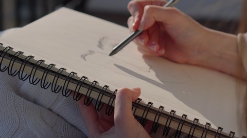 Close-up shot of woman artist drawing female portrait in sketchbook outdoor