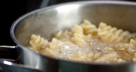 Fusilli pasta is boiled in boiling water in pan. Slow rotation.Macro background.
