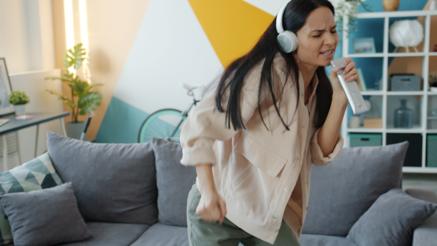 Slow motion of happy young lady in headphones dancing and singing in remore control having fun in apartment. People, lifestyle and joy concept. | Shutterstock HD Video #1055921918