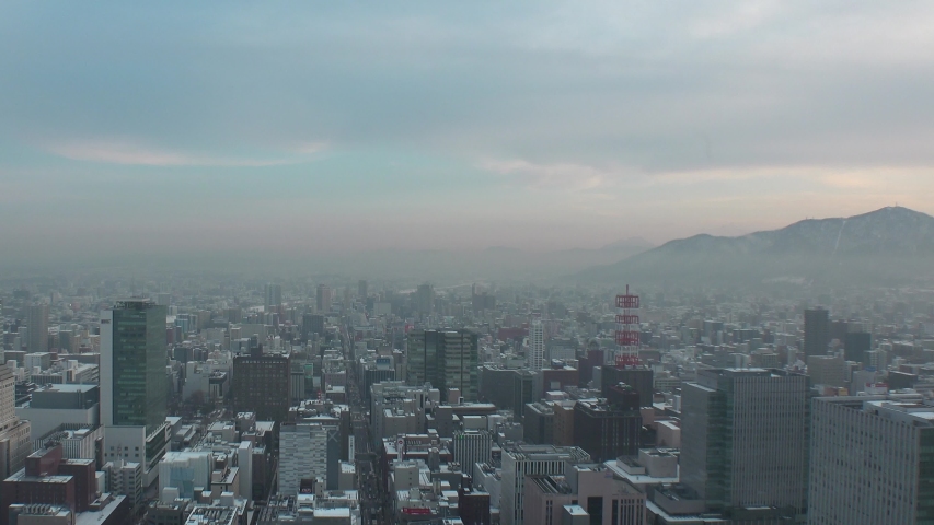 SAPPORO, HOKKAIDO, JAPAN - FEB 2020 : Aerial high angle sunset view of cityscape of Sapporo city. View of buildings and street traffic around Susukino downtown area. Time lapse shot sunset to night.