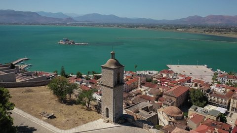 Aerial drone rotational video from medieval old clock tower in Acronafplia castle overlooking historic and picturesque seaside old town of Nafplio, Argolida, Peloponnese, Greece