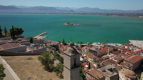 Aerial drone fly through video from medieval old clock tower in Acronafplia castle overlooking historic and picturesque seaside old town of Nafplio, Argolida, Peloponnese, Greece