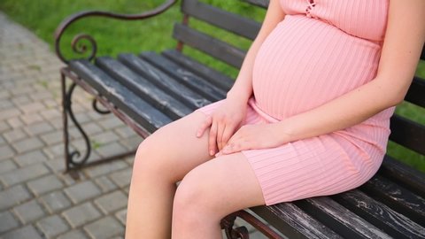Pregnant woman hands doing message of swollen leg on park bench