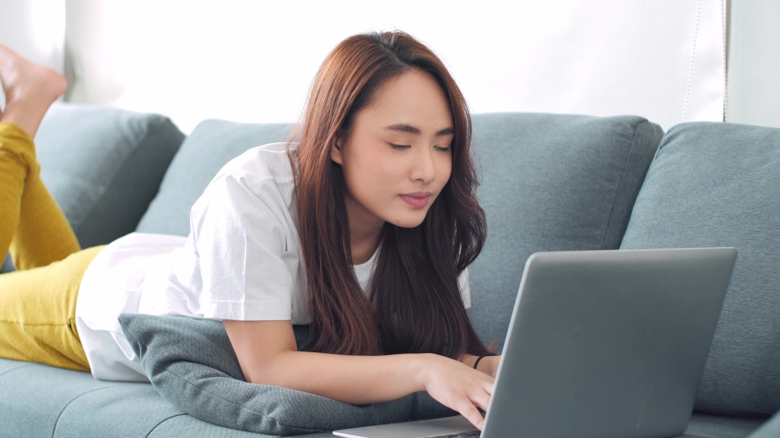 Young Asian female lying on the floor in the living room at home working with her laptop computer. | Shutterstock HD Video #1055928845