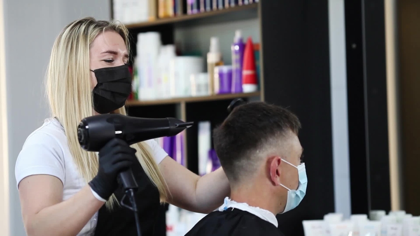 A hairdresser with security measures for Covid-19, blow-dry a man in a medicine mask, social distance, cutting hair with a medical mask and rubber gloves in a beauty salon Royalty-Free Stock Footage #1055929307