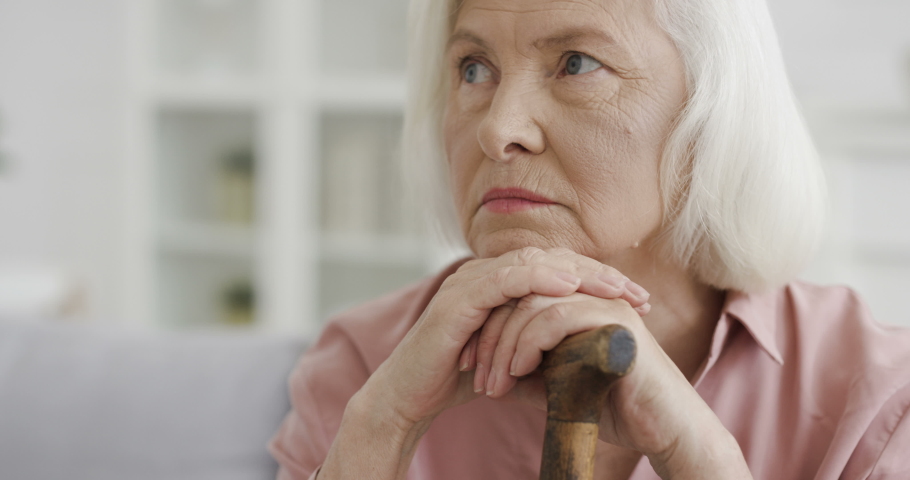 Portrait of Caucasian old wise beautiful woman looking at side and thinking with shrewd eyes while sitting on sofa in living room. Close up of serious senior grandmother with cane. Home resting. | Shutterstock HD Video #1055930681