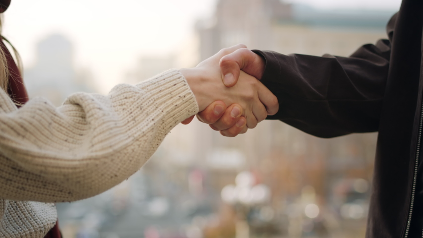 Closeup people shaking hands outdoors. Unrecognizable man and woman hands greeting in urban background. Unknown hipster couple meeting on city street. Young couple shaking hands outside | Shutterstock HD Video #1055931377