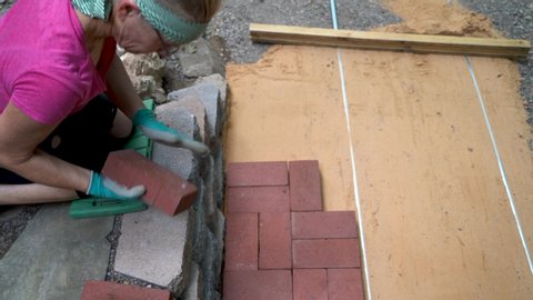 Overhead view of woman’s hand putting brick pavers onto a sand base for a patio construction.