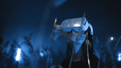 portrait of girl in VR headset or glasses looking around at night in nature in forest or field, modern technologies of virtual or augmented reality 3D graphics and holographic projection