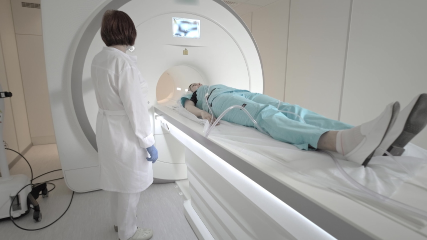 The doctor performs an MRI scan for a patient at the clinic. The girl lies in the MRI device. Magnetic resonance imaging in the study of the human body. Modern technologies in medicine. | Shutterstock HD Video #1055942567