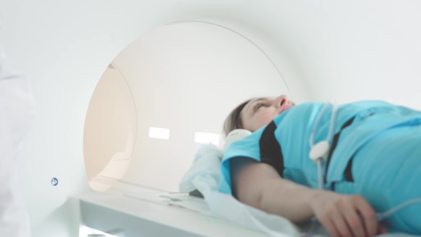 The doctor performs an MRI scan for a patient at the clinic. The girl lies in the MRI device. Magnetic resonance imaging in the study of the human body. Modern technologies in medicine. | Shutterstock HD Video #1055942588