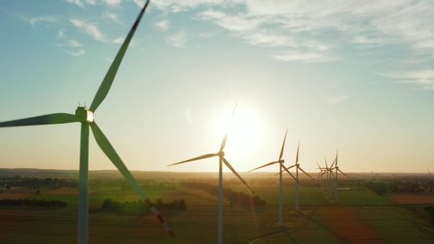 Drone Flies Over a Windmill Park at Sunset. Aerial View of a Farm With Wind Turbines Standing on a Wheat Field. Wind Power Turbines Generating Clean Renewable Energy for Sustainable Development.