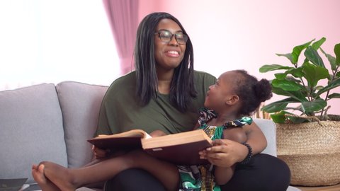 african american mother reading a book to her little daughter on couch at home . black girl lying on her mom study at home on sofa together . quarantine Home School 