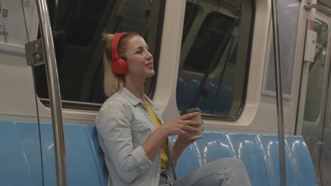 Portrait of young woman with headphones dancing music, singing and public transport funny. She drinks coffee.
